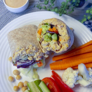 cut open wrap showing chickpea filling with assorted veggies on white plate with extra veggies on the side