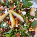 sliced pears on arugula in bowl with cranberries, walnuts and feta