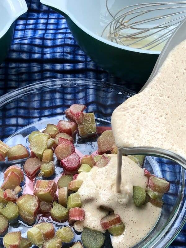 pouring batter over top of rhubarb in a hot baking dish