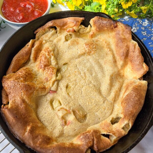 puffed oven pancake in cast iron pan with bits of rhubarb showing