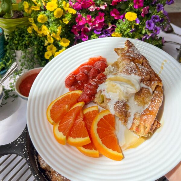 piece of rhubarb puffed pancake on plate with fruit sauce, whipped cream and syrup