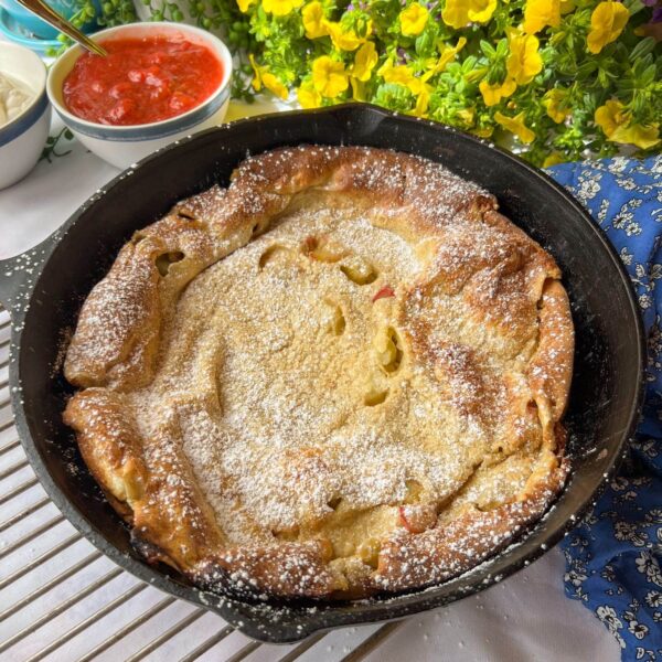 puffed oven pancake with rhubarb and powdered sugar in cast iron pan
