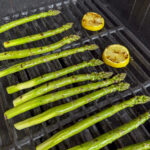 thick asparagus spears on grill with lemon slices also on grill faint char marks showing