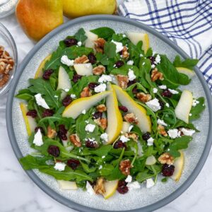 pears on top of arugula in bowl with feta, cranberries and walnuts