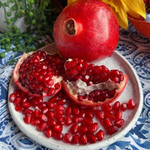 whole pomegranate, segmented pomegranate and pomegranate seeds on blue and white table cloth