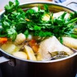 raw chicken pieces with vegetables and herbs in large soup pot with water