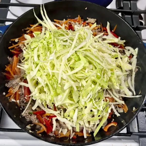 big pile of cabbage ontop of cooked ground meat and veggies in large pan on stove