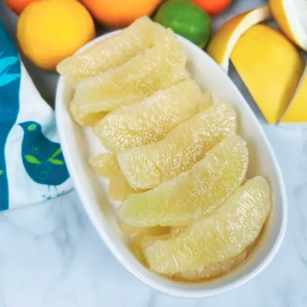 a white bowl on counter with large successfully peeled pomelo wedges
