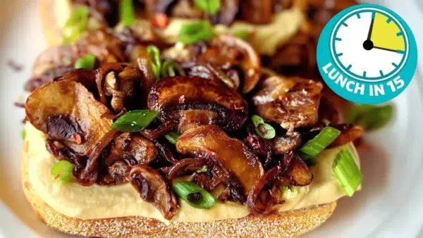 Close up of golden brown sauteed mushrooms and onions on toast loaded with hummus on white plate with clock face showing 15 minutes