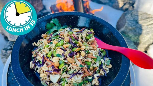 a metal camping style plate with an asian style coleslaw with peanuts and edamame beans held close to a campfire