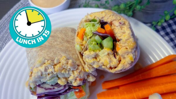 a full wrap cut in half exposing the chickpea and vegetable filling inside on a plate with carrots and other vegetables