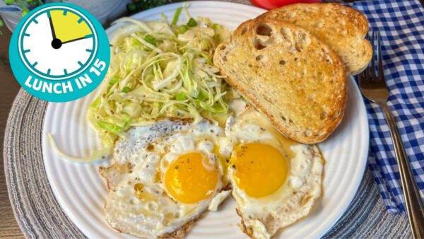 two sunny side up fried eggs with two pieces of rye toast and a side of crisp fried cabbage on a white plate