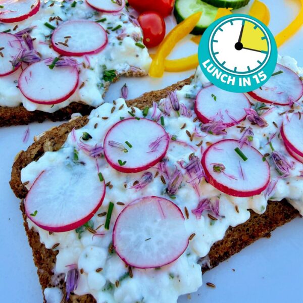 cottage cheese with herbs on pumpernickel bread topped with sliced radishes, chive blossoms and caraway seeds