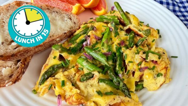 pillowy eggs with pieces of asparagus embedded with green chives and purple chive blossoms on top on white plate