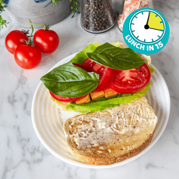 toasted rye bread with mayo on one side with two big basil leaves on top of tomatoes, cheese and lettuce on another piece of rye toast