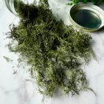 small dried dill fronds spilling out of jar on white table