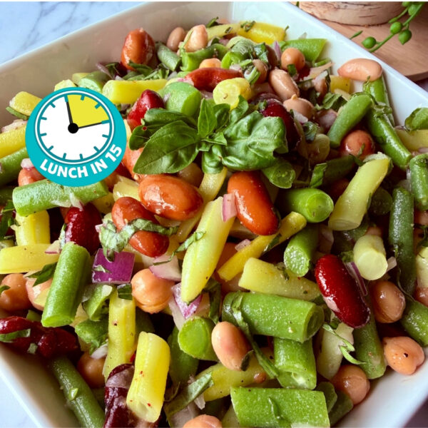 green and yellow beans, kidney beans, chickpeas and red onion tossed with fresh basil leaves in a white square dish