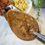 brown mushroom sauce in gravy boat with schnitzel and spaetzle in background